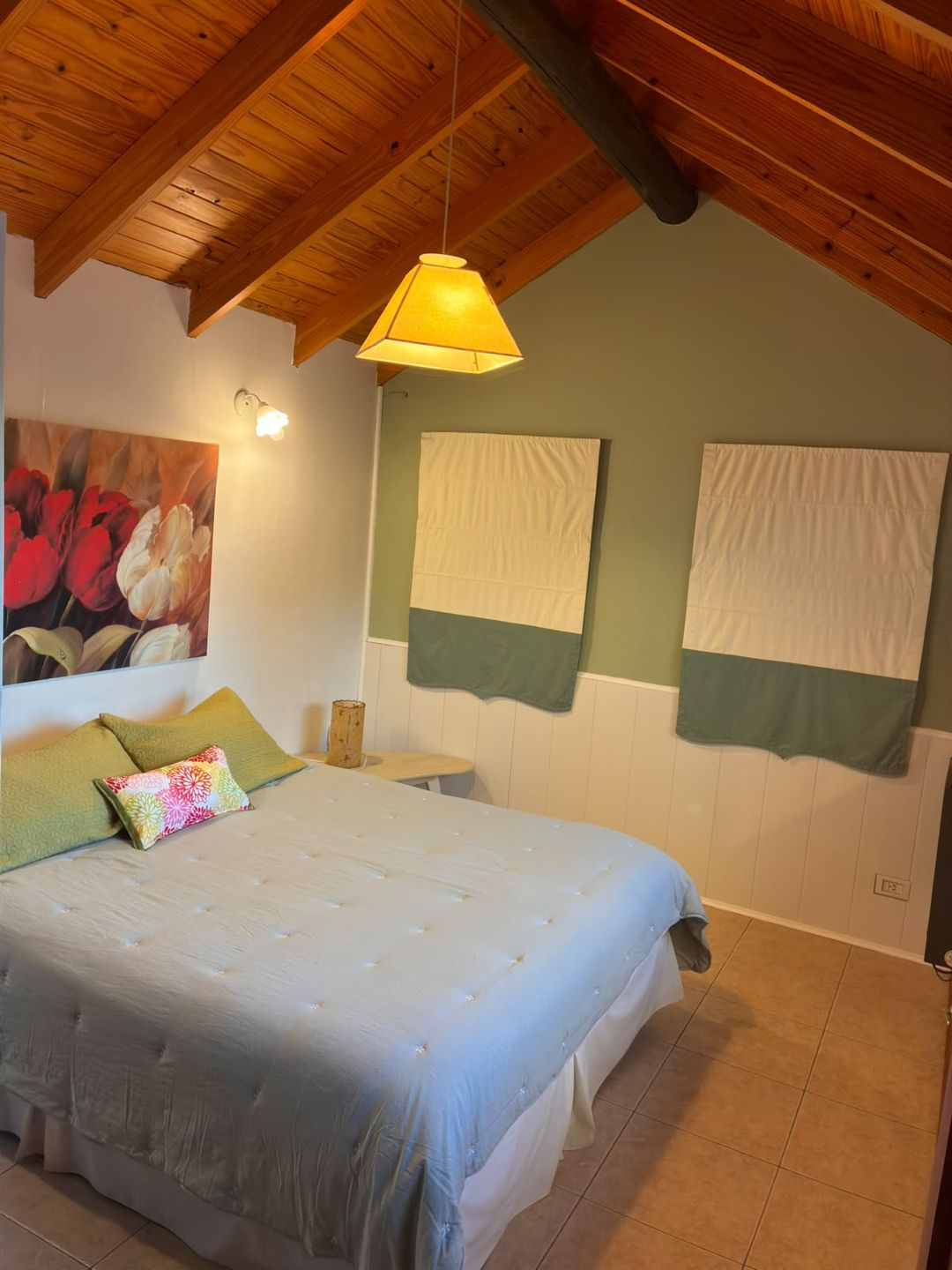 Dormitorio con cama matrimonial y techo de madera a dos aguas
